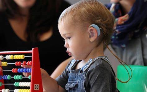 An audiologist showing a child and caretaker a hearing aid